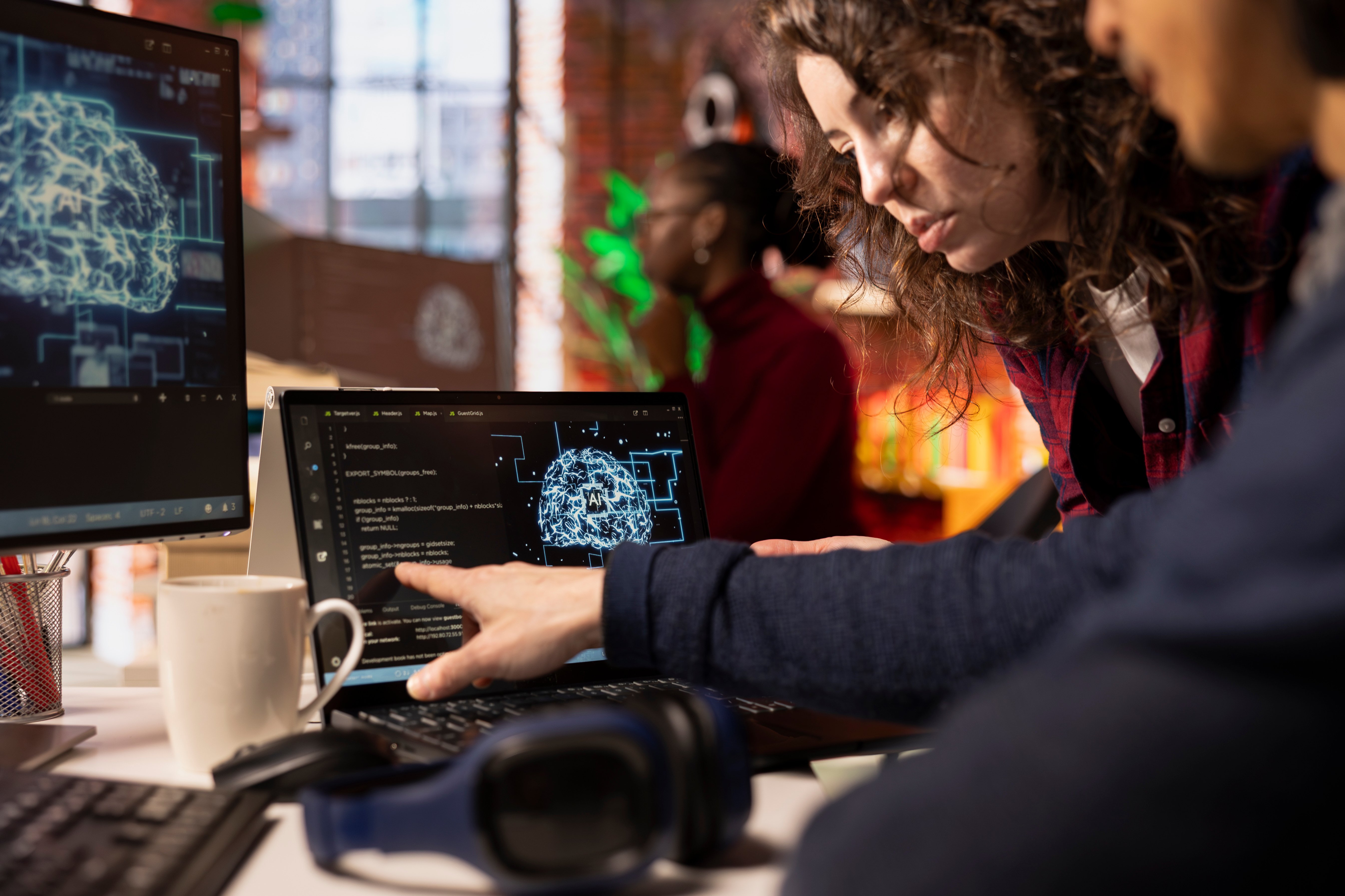 Two software developers collaborating on artificial intelligence programming, analyzing neural network visuals and code displayed on a computer screen in a modern tech workspace.
