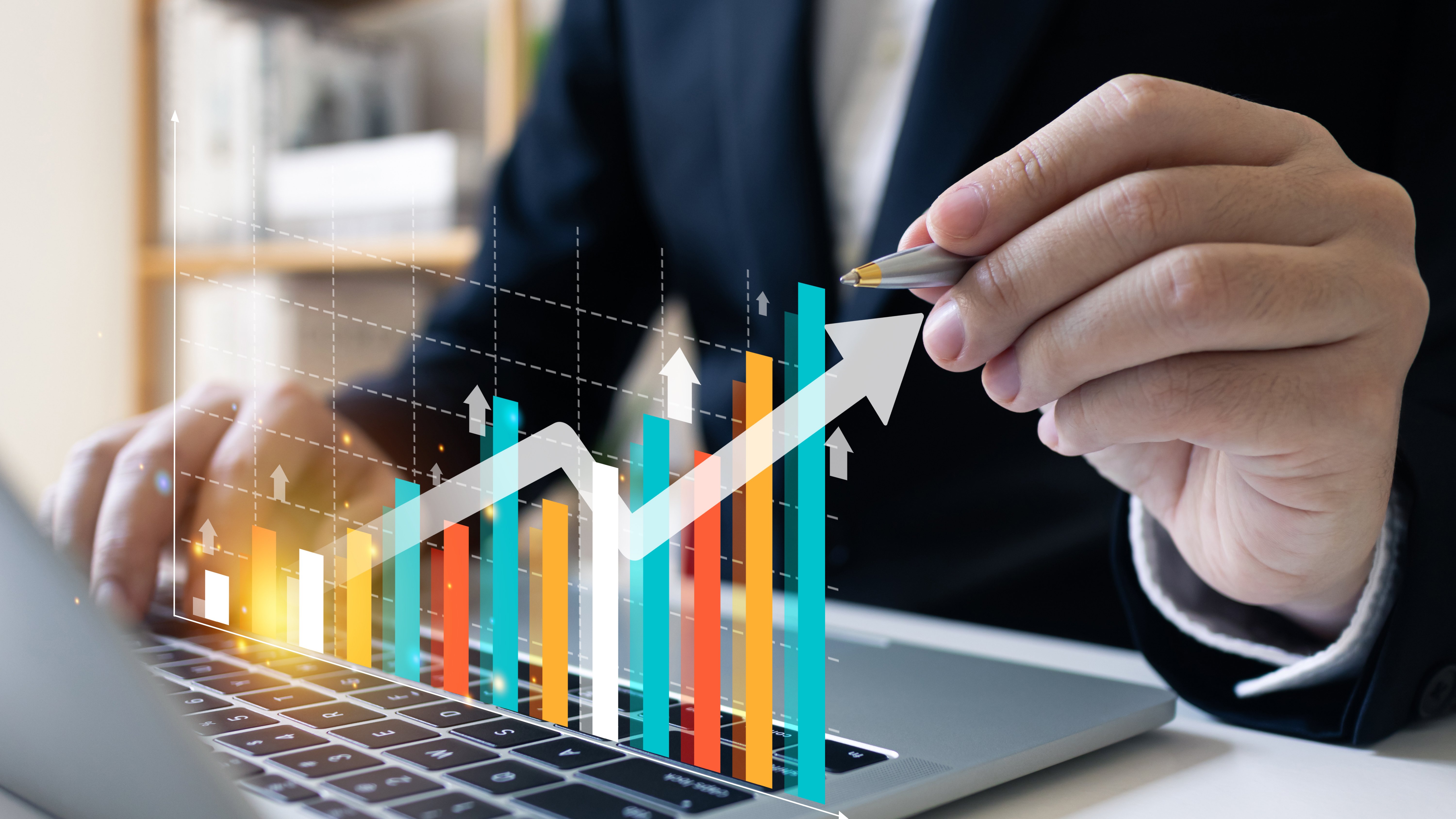 A business professional using a laptop while analyzing a colorful bar and line graph overlayed with upward-pointing arrows, symbolizing financial growth and data analytics.