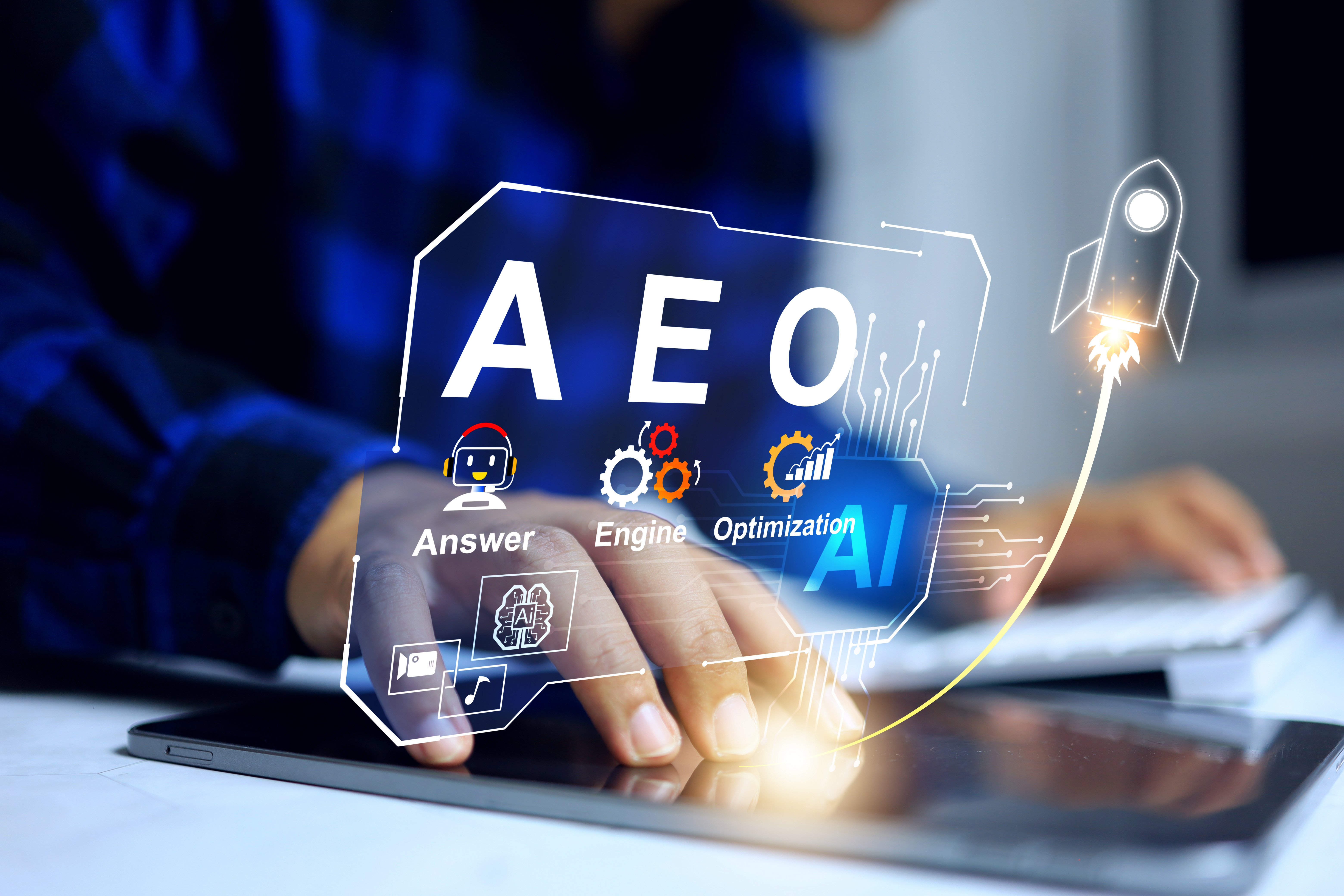 Person using a tablet with a futuristic digital overlay showing the acronym “AEO” for Answer Engine Optimization, along with AI-related icons such as gears, charts, and a rocket symbolizing innovation and growth in artificial intelligence technology.
