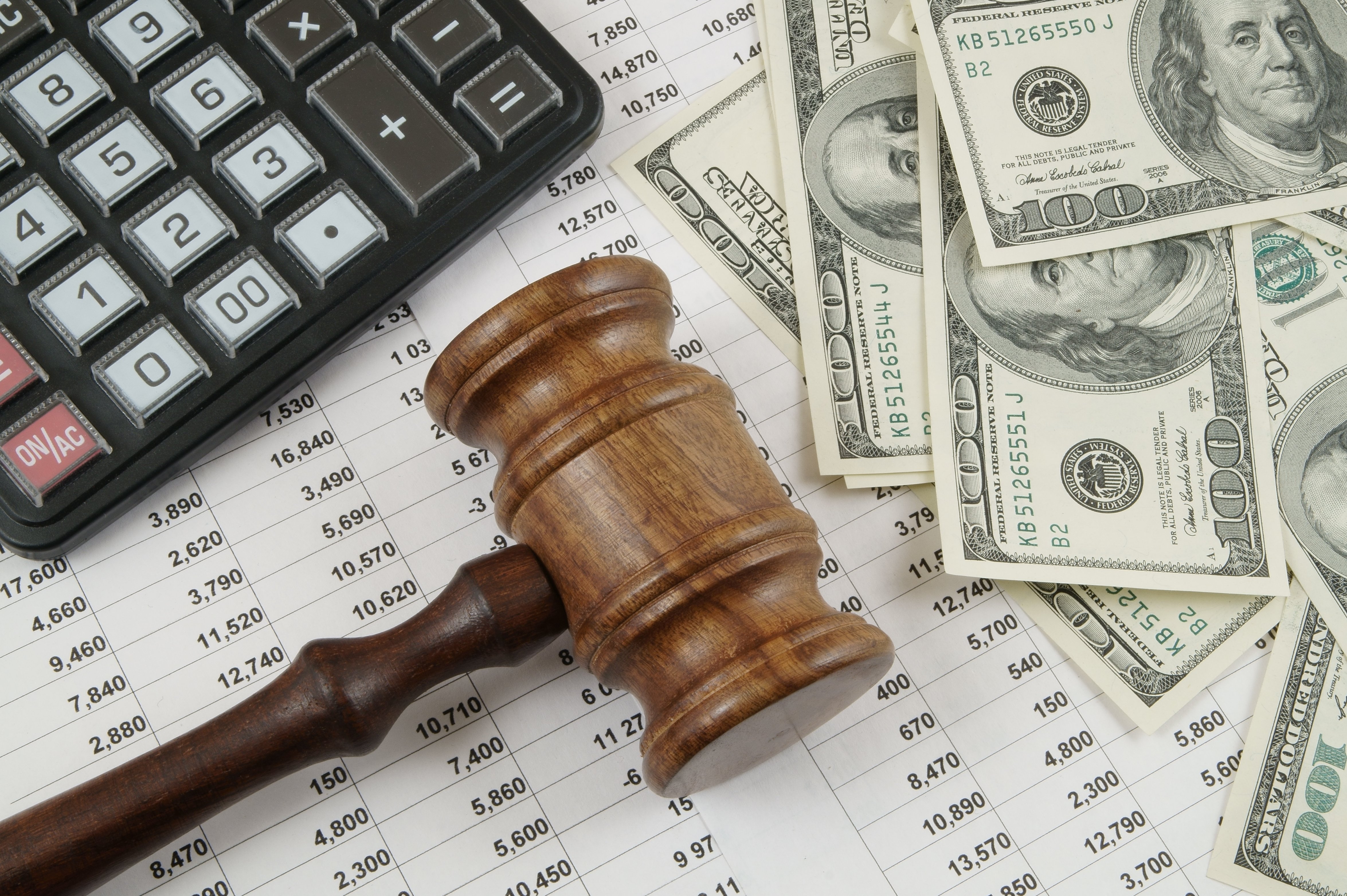 Judge’s gavel placed on financial documents with a calculator and scattered U.S. hundred-dollar bills, symbolizing legal costs, financial penalties, or settlements