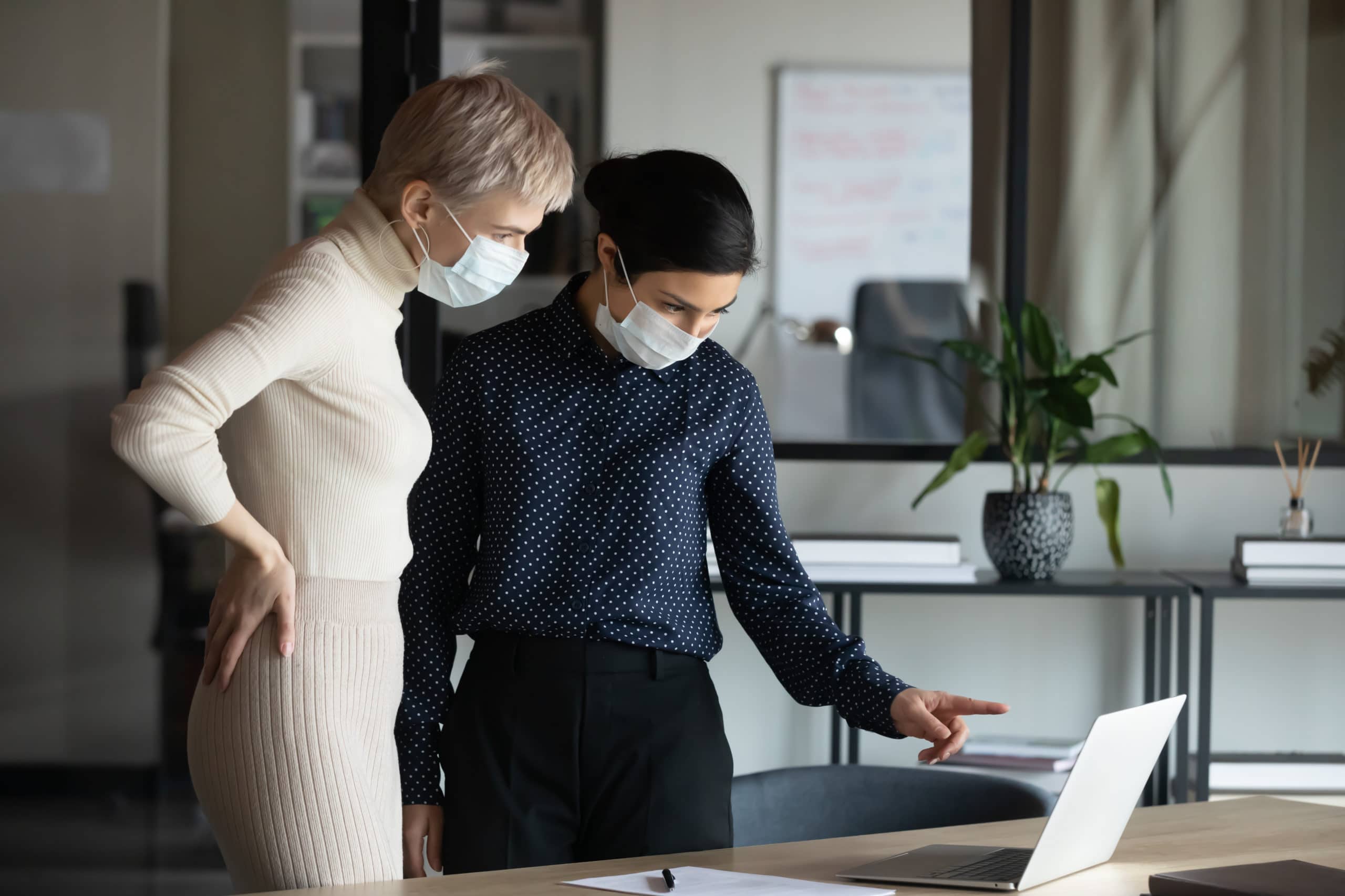 Two women in business attire looking at a laptop. 