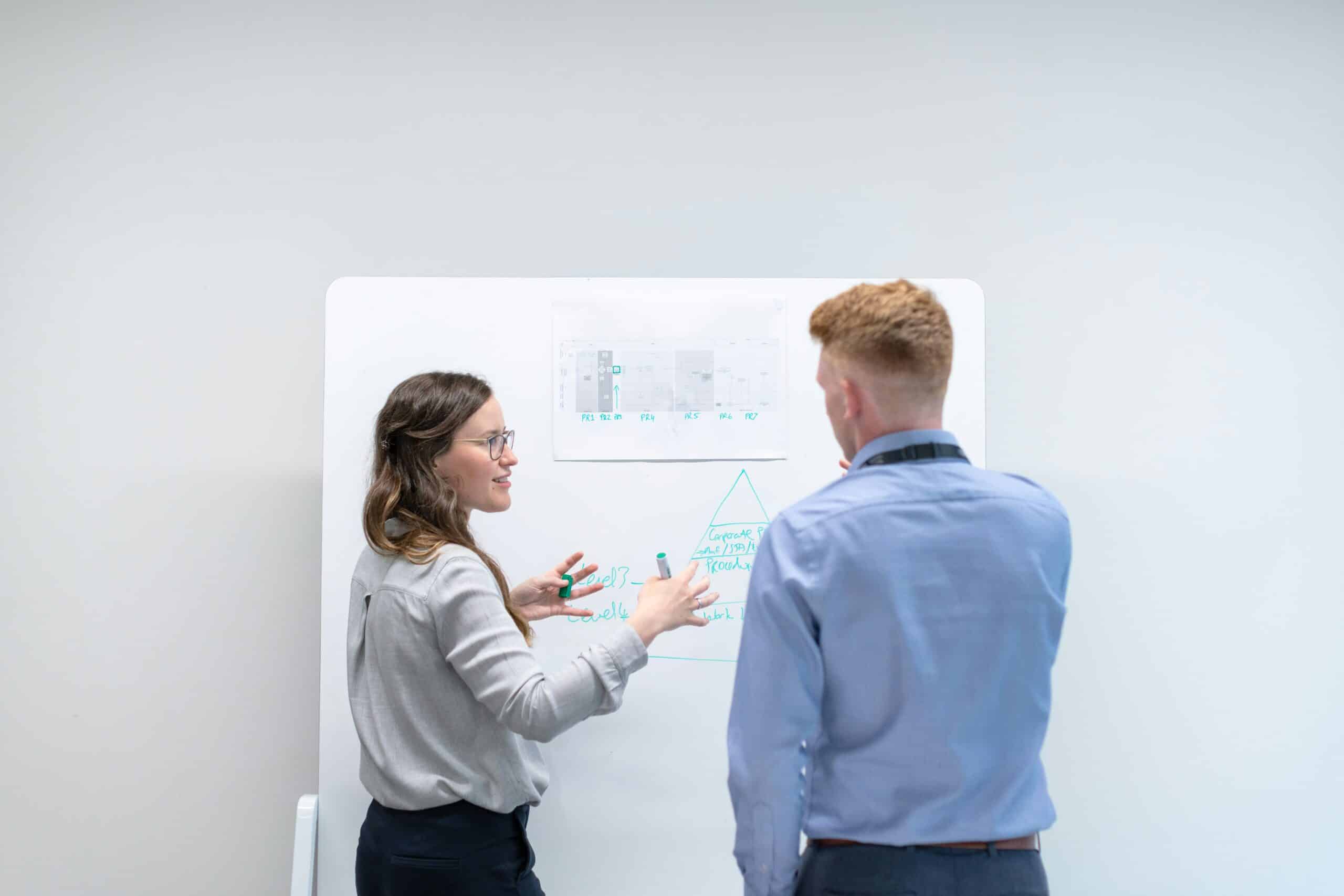 Data literacy for leaders: How to read, interpret, and act on your marketing insights 1 A woman, standing in front of a whiteboard, explaining concepts of data literacy to a man in a blue shirt.
