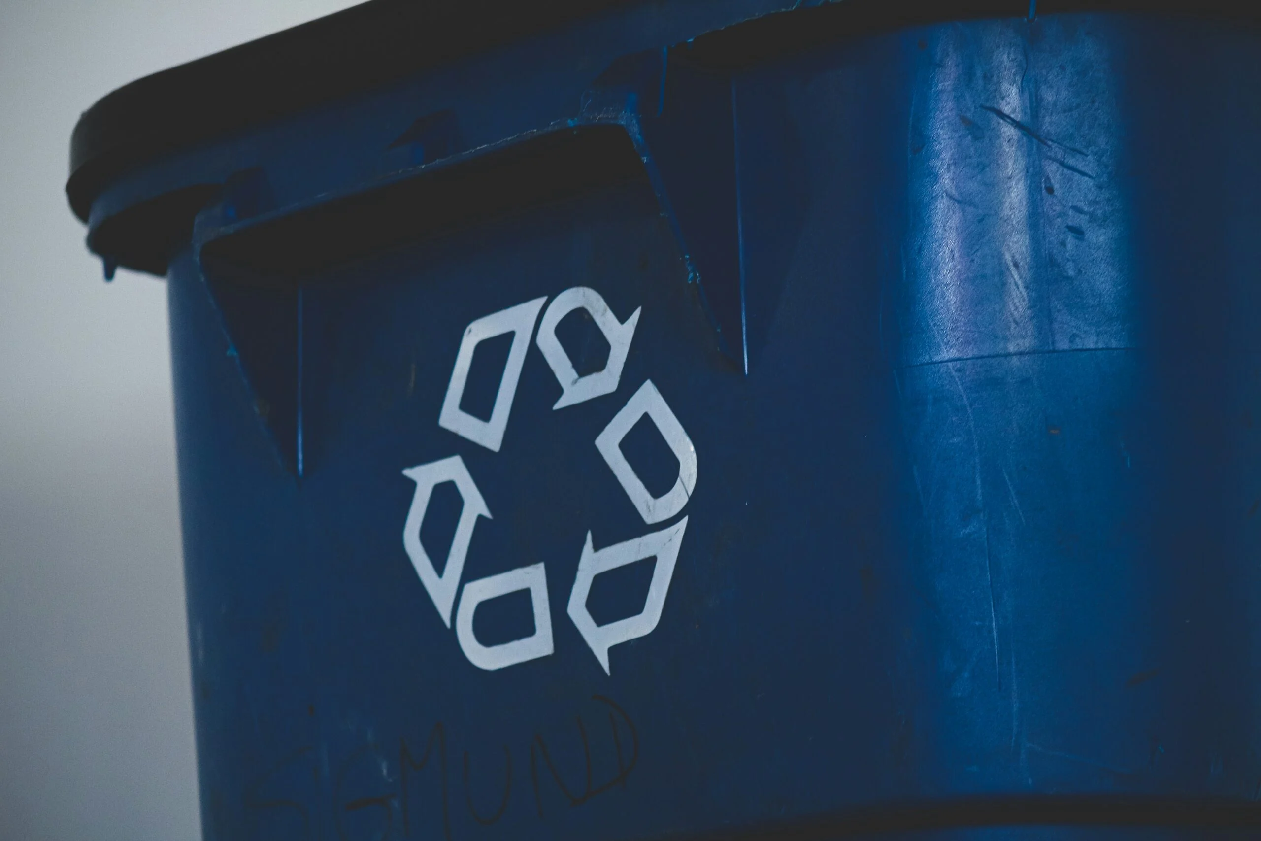 Photograph of a blue bin with the recycling symbol on it.