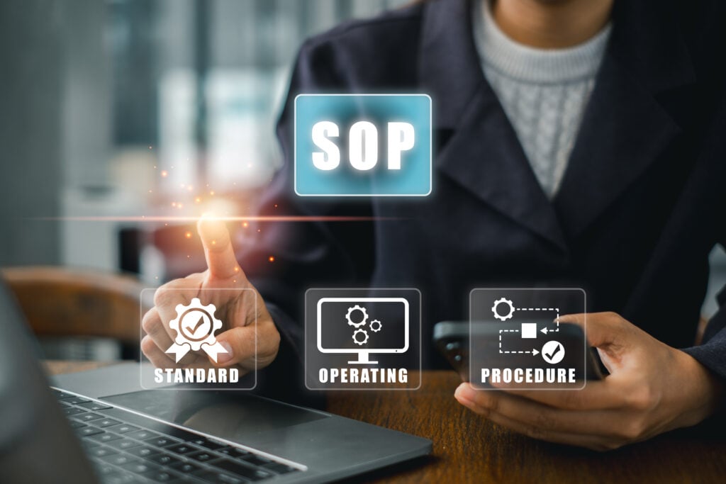Curating a Source of Truth for Your Operations 2 Business professional using a smartphone and laptop while selecting a glowing “SOP” icon, with graphics representing standard operating procedures, processes, and compliance.