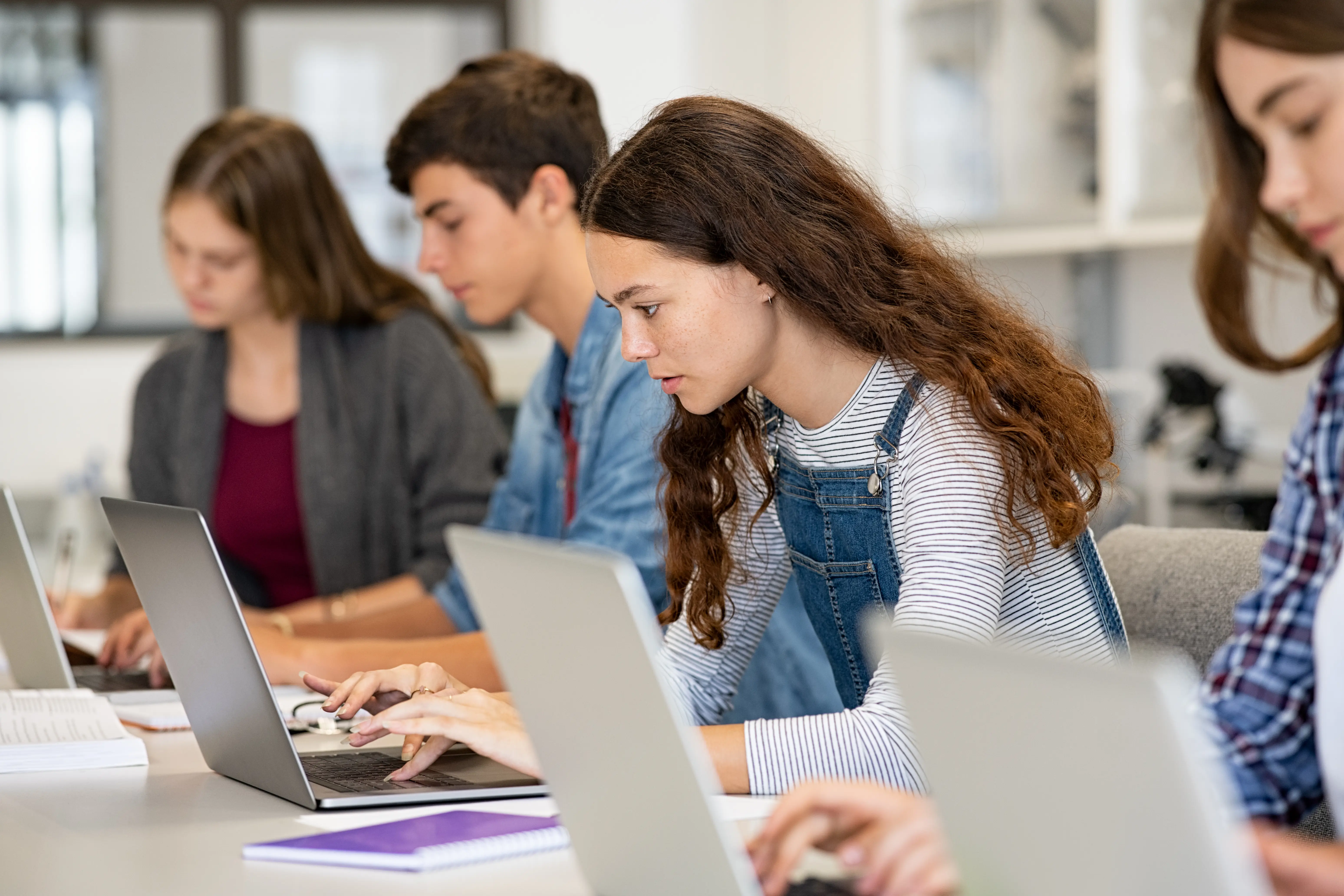 What Students Are Asking Us About AI 2 በዘመናዊና ብሩህ ክፍል ውስጥ በላፕቶፖች ላይ የሚሰሩ የሁለተኛ ደረጃ ተማሪዎች ረድፍ፣ አንዲት ሴት ተማሪ ትኩረት በትኩረት ስትጽፍ፣ እኩዮቿ አብረዋት ሲሰሩ።