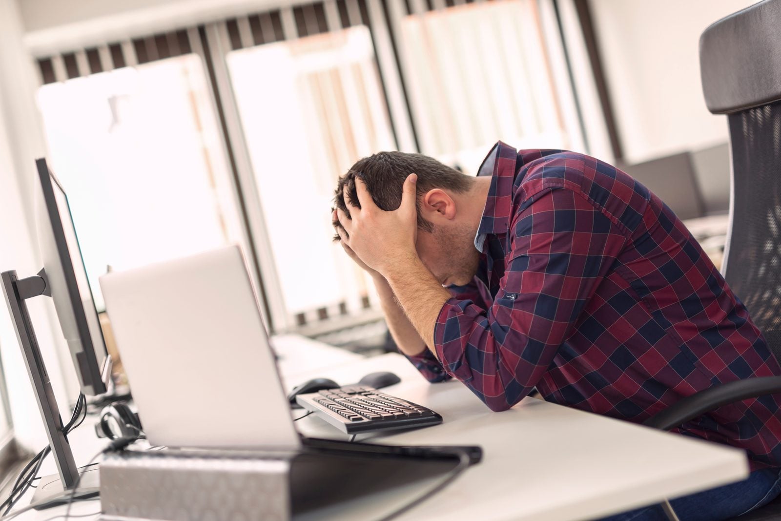 How Many Skill Sets It Takes to Run a Successful Marketing Campaign 2 Overwhelmed marketing professional sitting with head in hands at a desk in front of a laptop, representing burnout from trying to do it all